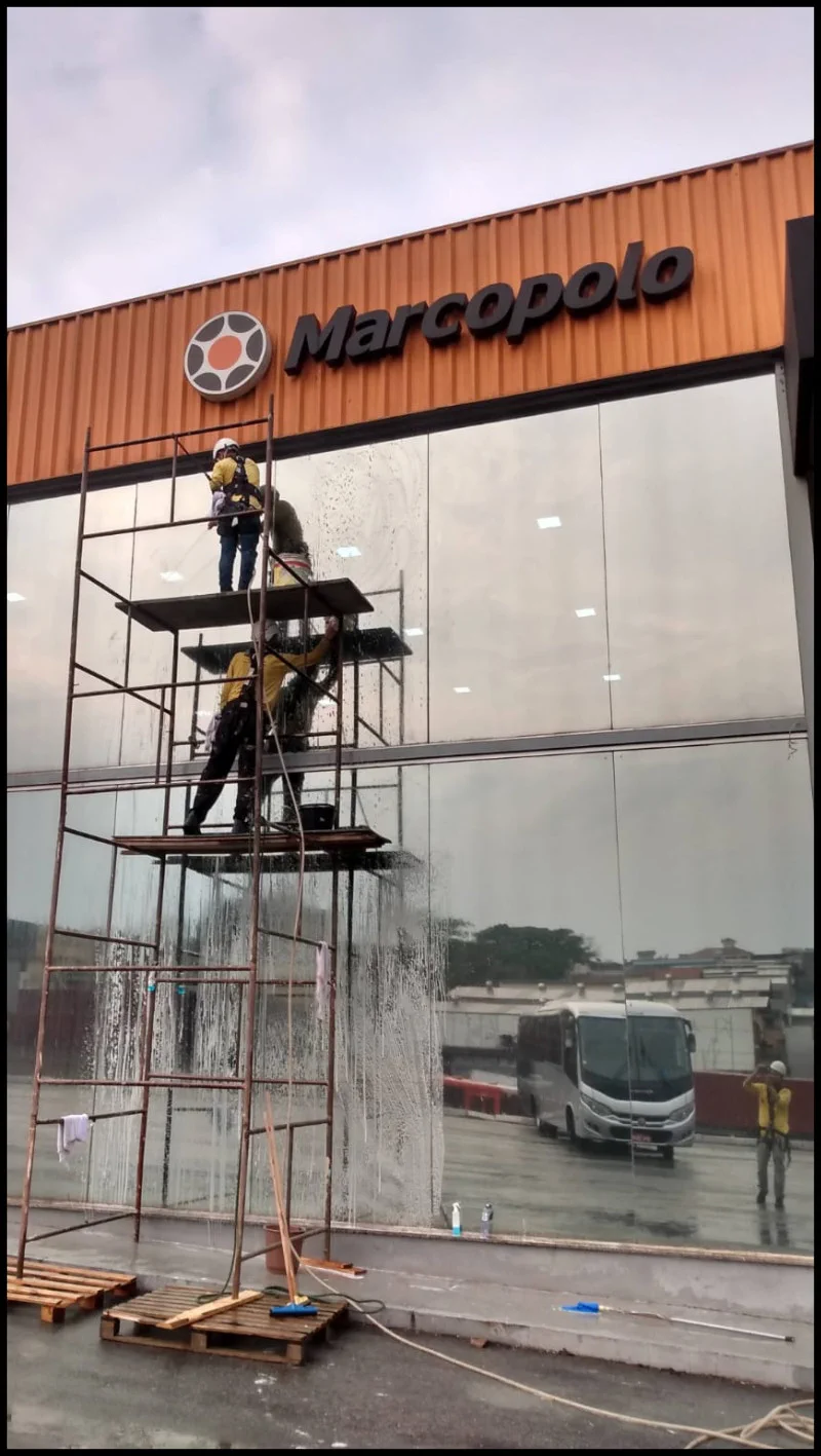 Dois profissionais limpam uma fachada de vidro com apoio de andaime
